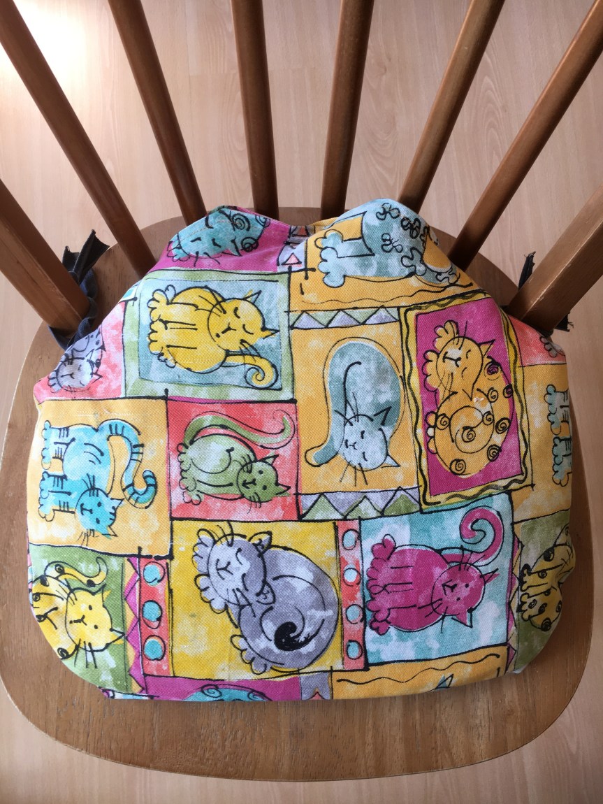 Seat cushion on wooden chair. The cushion is made from fabric covered in cartoon images of cats.